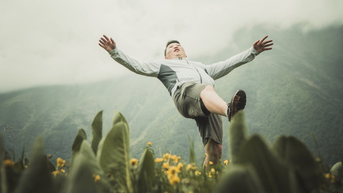 woman in white long sleeve shirt and black pants jumping on green grass field during daytime